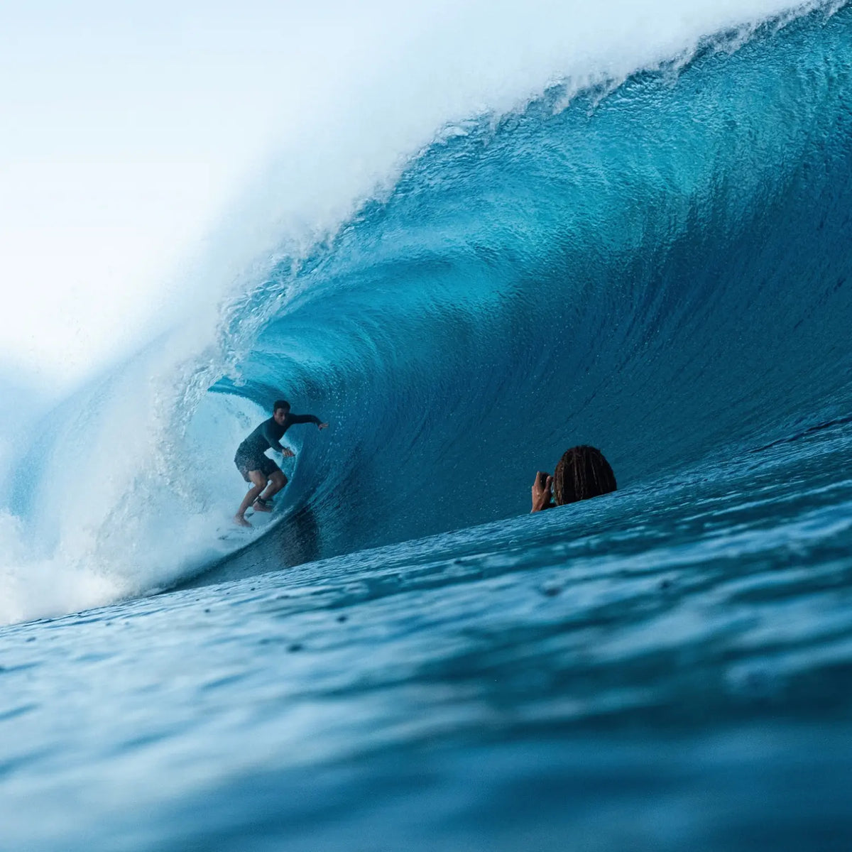 A surfer riding a large wave with another person in the water.