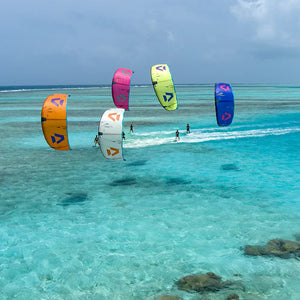 Kitesurfers on turquoise water with colorful kites against a cloudy sky.