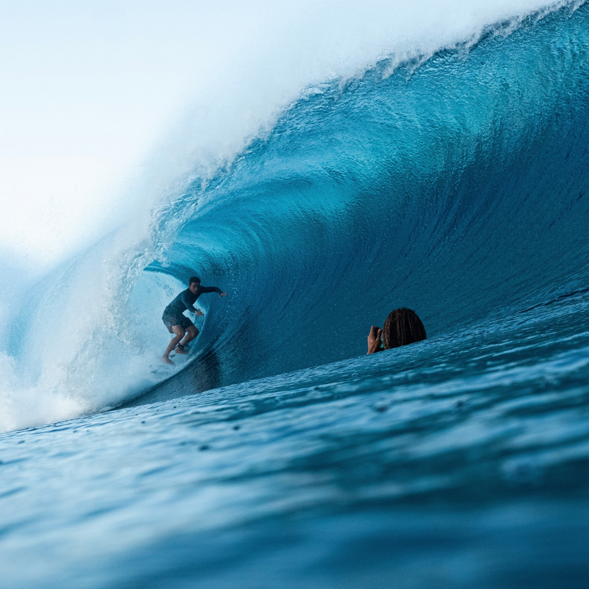 A surfer riding a large wave with another person in the water.